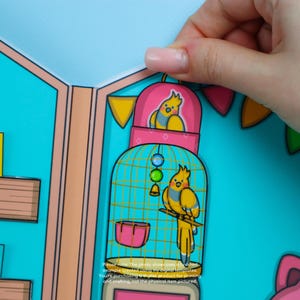 May include: A paper craft featuring a yellow bird in a pink and teal birdcage. The birdcage has a teal base and a pink top. The image includes text that reads, "Please note. The photo showcases a finished example created using my digital templates."
