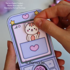 May include: A paper craft mobile phone featuring a light purple frame with yellow stars and pink hearts. A small cartoon cat illustration is positioned on the screen. The text reads: This is a Digital Product - Please Read the Full Description Before Purchase.