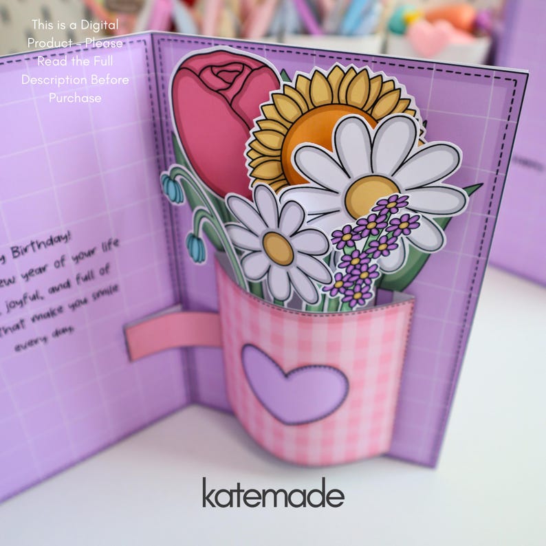 May include: A handmade greeting card with a pop-up floral arrangement. The card features a pink gingham mug with a heart, holding a pink rose, sunflower, daisies, and purple flowers. The card is lavender with the text "katemade".