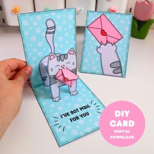May include: A handmade pop-up card featuring a gray cartoon cat holding a pink envelope with a heart. The card has a light blue background with paw prints and the text "I've got mail for you." A pink circle with "DIY CARD DIGITAL DOWNLOAD" is also visible.