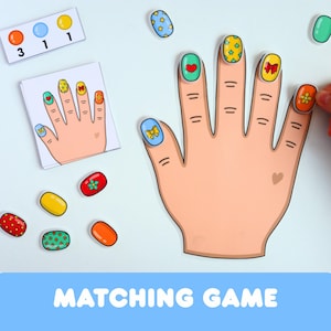 Könnte beinhalten: Ein Zuordnungsspiel mit einer Hand aus Papier und magnetischen oder klebenden Nagelstücken. Das Set enthält eine Referenzkarte mit einer Hand mit verzierten Nägeln, lose bunte Nagelstücke mit verschiedenen Mustern und eine kleine Zahlentabelle.