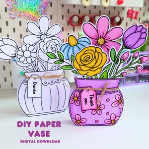 Könnte beinhalten: Zwei Papier-Vasen-Bastelsets mit Blumenarrangements. Eine Vase ist weiß mit schwarzen Umrissen und einem "Danke"-Schild. Die andere ist lila mit rosa Blumen, einer gelben Rose, einer blauen Blume und einem "Thank you"-Schild. Beide haben Bindfaden.