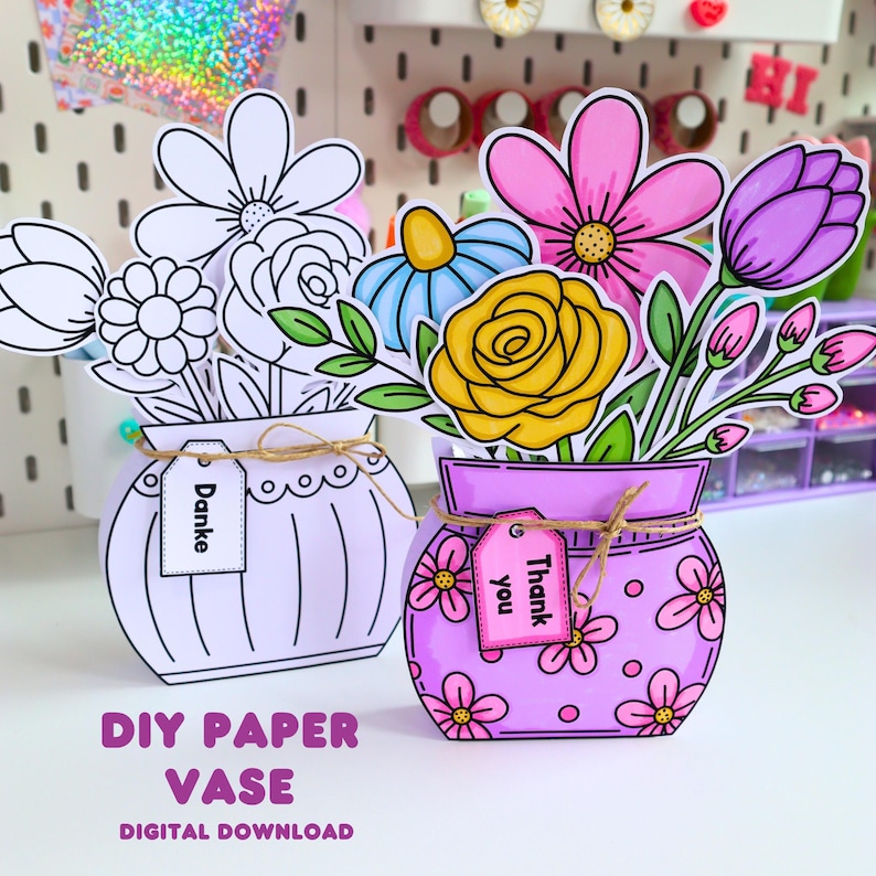 May include: Two paper vase crafts with floral arrangements. One vase is white with black outlines and a tag reading "Danke". The other is purple with pink flowers, a yellow rose, a blue flower, and a tag reading "Thank you". Both have twine.
