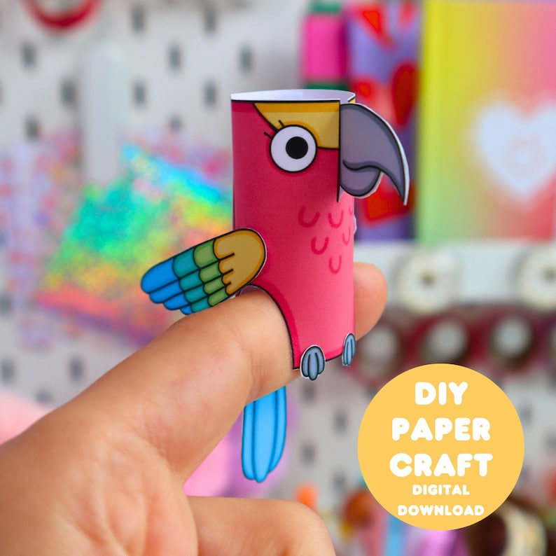 May include: A paper finger puppet shaped like a parrot with a pink body, yellow forehead, grey beak, and blue and green wings. The puppet features a cartoon-style design with large eyes and a long blue tail. A yellow circular graphic reads DIY PAPER CRAFT DIGITAL DOWNLOAD.
