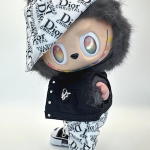 May include: A collectible figurine wearing a black jacket, pants, and shoes, all adorned with the "Dior" logo in white on a black background. The figurine has a furry hood and hat, and its eyes have a rainbow effect.