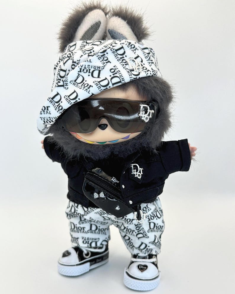 May include: A plush toy dressed in a black jacket, white pants, and sneakers, all adorned with the "Dior" logo. The toy wears sunglasses, a hat, and a fanny pack, also branded with the same logo. The toy has a furry head with bunny ears.