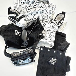 May include: A collection of miniature fashion accessories, including black and white sneakers, a black beanie, a small black purse, and black pants. The items feature the "Dior" logo and branding.