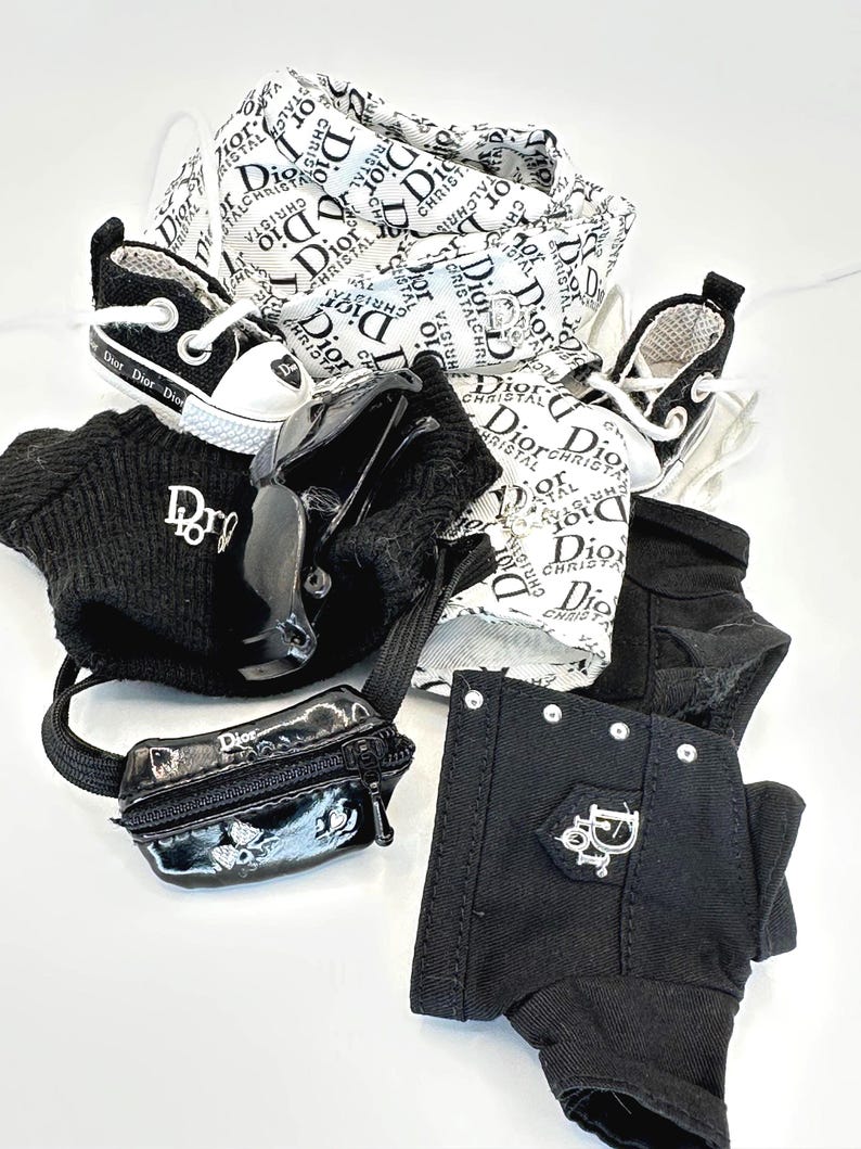 May include: A collection of miniature fashion accessories, including black and white sneakers, a black beanie, a small black purse, and black pants. The items feature the "Dior" logo and branding.