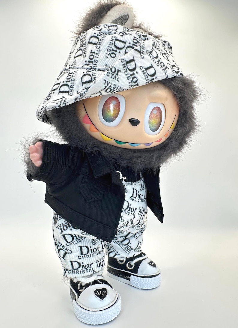 May include: A whimsical figurine dressed in a black jacket, pants, and sneakers, all adorned with the "Dior" logo. The figure has a colorful face, a furry head, and a matching hat. The sneakers have white soles.
