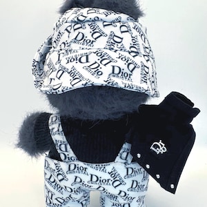 May include: A plush toy dressed in a black and white outfit with the "Dior" logo. The outfit includes a hat, overalls, jacket, and sneakers. The jacket has a "Dior" logo and rhinestone accents.