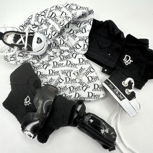 May include: A collection of miniature fashion items, including a black jacket, sneakers, and a small purse. The items feature the "Dior" logo in black and white. The sneakers have white laces and a heart design.