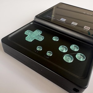 May include: A black handheld gaming device with a screen and a control pad. The device features a directional pad and several buttons in a light green color. The screen displays a time of 4:50 PM. The device is open, revealing the screen and controls.