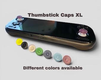 May include: A black handheld gaming console with two purple thumbstick caps installed. Below the console, seven additional thumbstick caps are arranged in a row in yellow, black, beige, green, dark grey, light blue, and pink. Text reads: Thumbstick Caps XL. Different colours available.