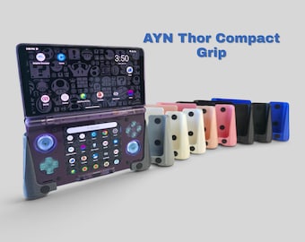 May include: A handheld gaming console with a translucent purple shell and blue joysticks, fitted with a dark gray ergonomic grip. Beside it, a row of AYN Thor Compact Grip accessories in various colors including white, pink, black, and blue.