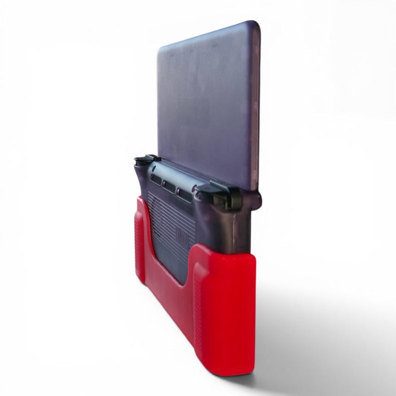 Puede incluir: Una consola de juegos port&aacute;til con una carcasa de color morado oscuro transl&uacute;cido y una funda protectora de color rojo vibrante. El dispositivo se muestra desde un &aacute;ngulo lateral, destacando los botones superiores, las rejillas de ventilaci&oacute;n y la funda.