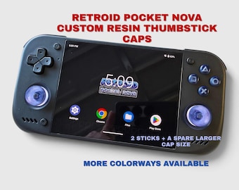 May include: A black handheld gaming console featuring custom translucent purple resin thumbstick caps. The screen displays the Retroid Pocket Nova interface with app icons. Text reads: RETROID POCKET NOVA CUSTOM RESIN THUMBSTICK CAPS, 2 STICKS + A SPARE LARGER CAP SIZE, MORE COLORWAYS AVAILABLE.