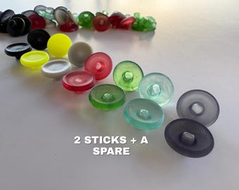 May include: A collection of round, multi-colored buttons in various shades including black, white, red, green, and yellow, arranged in a scattered pattern. The text 2 STICKS + A SPARE is printed in white at the bottom of the image.