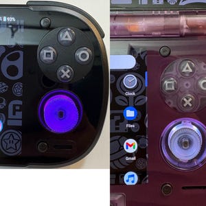 May include: Two handheld gaming devices, one black and one purple, with visible control buttons. The black device has a purple glowing joystick and a screen displaying app icons. The purple device also has a glowing joystick and a screen showing app icons.