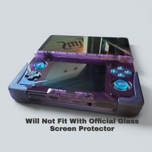 Puede incluir: Una consola de juegos port&aacute;til transl&uacute;cida de color p&uacute;rpura con una funda protectora oscura, joysticks azules y un pad direccional. La pantalla refleja la luz y el texto "Will Not Fit With Official Glass Screen Protector" aparece impreso debajo.