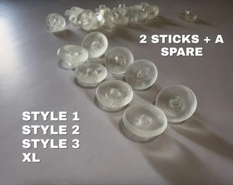 May include: A collection of clear, circular, textured buttons with a central protrusion. The image includes the text 2 STICKS + A SPARE, STYLE 1, STYLE 2, STYLE 3, and XL. The buttons are arranged in a group, showing a ridged edge pattern on each piece.