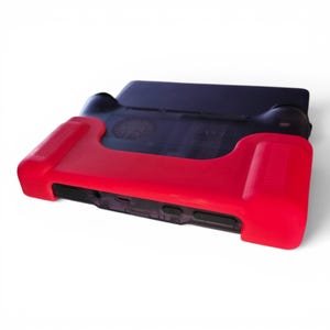 Puede incluir: Una consola de juegos port&aacute;til con una carcasa negra transl&uacute;cida y una funda protectora de silicona de color rojo brillante. El dispositivo incluye empu&ntilde;aduras de mando integradas en los laterales, botones visibles y puertos en el borde inferior.