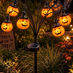 Peut inclure: Un piquet de jardin solaire avec six citrouilles lumineuses orange, chacune portant un chapeau de sorcière noir. Le support en métal noir possède des bras incurvés soutenant les citrouilles éclairées, avec un panneau solaire sur le mât.