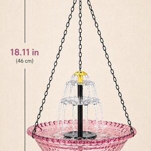 May include: A hanging fountain with a pink glass bowl featuring a textured rim and a central tiered water feature. It is suspended by black chains and a hook. The total height is 18.11 inches and the bowl diameter is 9.25 inches.