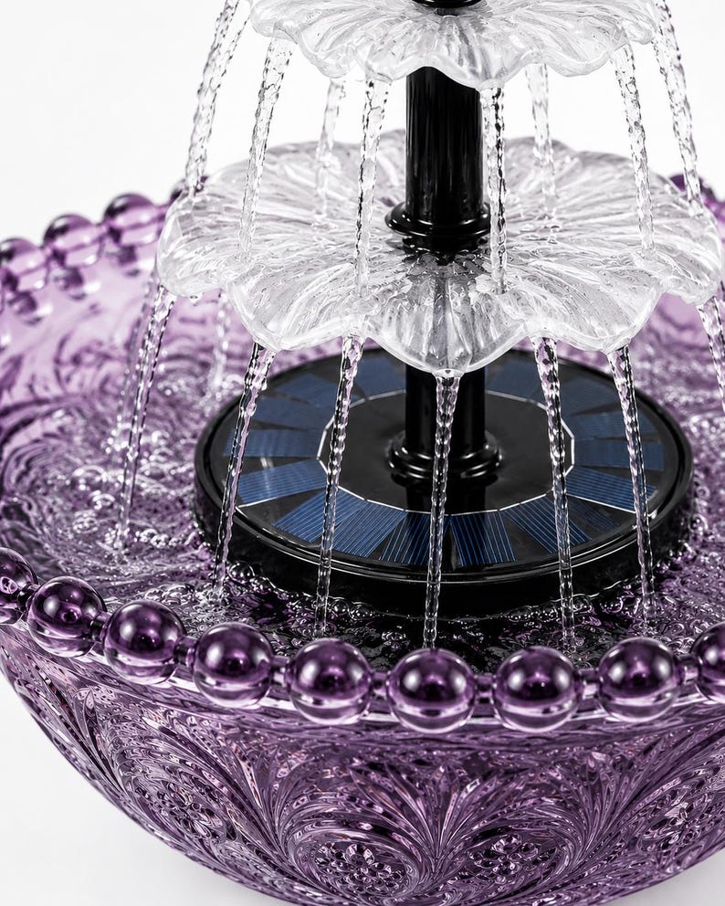 May include: A purple glass water fountain featuring a beaded rim and intricate embossed patterns. The fountain has a central black solar panel base with two clear, tiered, flower-shaped tiers that distribute water in a cascading circular motion.