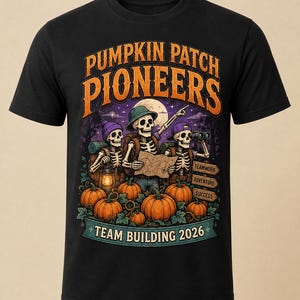 May include: A black t-shirt featuring a graphic of three skeletons in a pumpkin patch. The text reads PUMPKIN PATCH PIONEERS, TEAMWORK, ADVENTURE, SUCCESS, and TEAM BUILDING 2026. The skeletons wear hats and backpacks, holding a map, lantern, and binoculars.