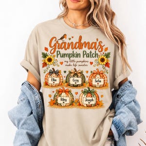 May include: A beige t-shirt featuring a graphic with the text Grandma's Pumpkin Patch and my little pumpkins make life sweeter. The design includes five pumpkins with the names Ellia, Cozy, Sofia, Riley, and Joseph, decorated with autumn leaves, sunflowers, and a small bird.