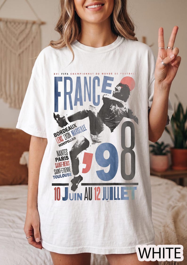 K&ouml;nnte beinhalten: Ein wei&szlig;es T-Shirt mit einem Grafikdruck f&uuml;r die FIFA Fu&szlig;ball-Weltmeisterschaft 1998 in Frankreich. Das Design enth&auml;lt den Text "FRANCE 98", "10 JUIN AU 12 JUILLET" sowie eine Liste franz&ouml;sischer St&auml;dte wie Bordeaux, Lens, Lyon, Marseille und Paris.