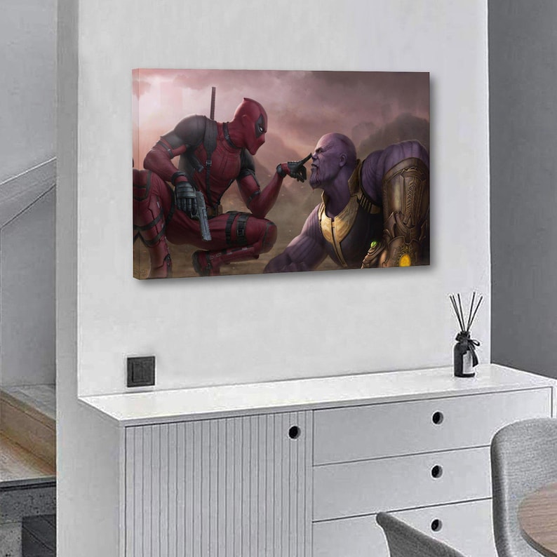 May include: Canvas art print featuring Deadpool and Thanos in a dramatic pose. Deadpool, in a red and black suit, points a gun at Thanos, who is in a purple and gold suit. The background is a hazy, mountainous landscape.