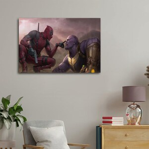May include: A canvas print featuring Deadpool and Thanos in a dramatic pose. Deadpool, in a red and black suit, points at Thanos's face. Thanos, with purple skin and gold armor, looks at Deadpool. The background shows a cloudy, mountainous landscape.