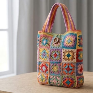 May include: A colorful, handmade crochet tote bag. The bag features a patchwork design with various square patterns in shades of blue, yellow, orange, and purple. It has a wooden button closure and matching crochet handles. The bag is sitting on a wooden surface.