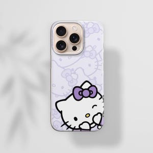 Puede incluir: Una funda de tel&eacute;fono de color lila claro con un dise&ntilde;o de Hello Kitty. La funda tiene un patr&oacute;n repetido de caras y lazos de Hello Kitty. La imagen principal es un primer plano de Hello Kitty gui&ntilde;ando un ojo con un lazo morado. La funda tiene una lente de c&aacute;mara dorada.