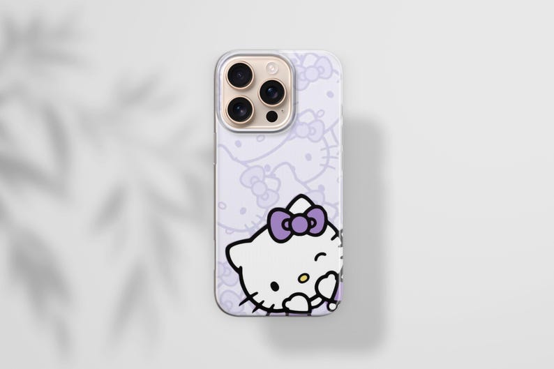 Puede incluir: Una funda de tel&eacute;fono de color lila claro con un dise&ntilde;o de Hello Kitty. La funda tiene un patr&oacute;n repetido de caras y lazos de Hello Kitty. La imagen principal es un primer plano de Hello Kitty gui&ntilde;ando un ojo con un lazo morado. La funda tiene una lente de c&aacute;mara dorada.