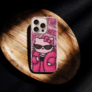 Puede incluir: Funda de tel&eacute;fono transparente con un dise&ntilde;o de Hello Kitty rosa. Hello Kitty lleva gafas de sol, un abrigo de piel rosa y un collar. El fondo tiene un efecto de purpurina rosa y un patr&oacute;n de billetes de d&oacute;lar.