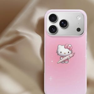 Puede incluir: Funda de tel&eacute;fono rosa con un personaje de dibujos animados sosteniendo un objeto enrollado. La funda tiene un fondo degradado rosa claro con acentos blancos en forma de estrella. El &aacute;rea de la c&aacute;mara es plateada.