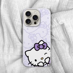 Puede incluir: Una funda de tel&eacute;fono lavanda con un dise&ntilde;o de Hello Kitty blanco y un lazo morado. La funda tiene un patr&oacute;n repetido de caras y lazos de Hello Kitty. La funda del tel&eacute;fono tiene un recorte para la c&aacute;mara y est&aacute; sobre una superficie blanca texturizada.