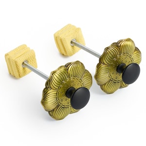 May include: Two fire poi with a floral design. The heads are gold with black knobs, and the wicks are yellow. The wicks are attached to the floral heads with a silver rod. The poi are set against a white background.