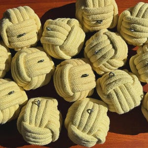 May include: A collection of yellow rope knots with metal rings. The knots are tightly woven, and the metal rings are inserted through the center of each knot. The knots are arranged on a wooden surface.