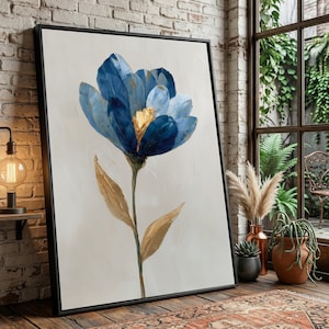 May include: Large framed canvas art depicting a stylized blue flower with gold highlights. The flower has multiple layers of petals against a neutral backdrop. The artwork is displayed in a room with natural light and a brick wall.
