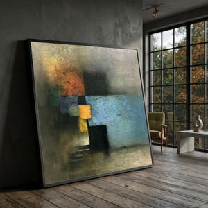 May include: A large square abstract painting in a black frame featuring a textured composition of dark gray, black, and muted earth tones. The artwork includes geometric blocks of vibrant orange, bright yellow, and light blue paint.