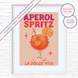 May include: A pixel art cross stitch pattern featuring an orange cocktail in a stemmed glass with an orange slice garnish. The text reads APEROL SPRITZ and LA DOLCE VITA in red and orange block letters against a light peach background.