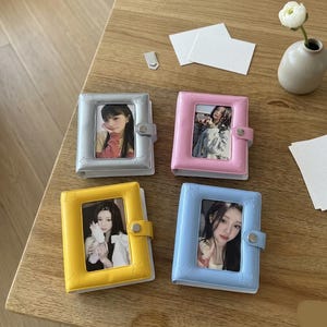 Peut inclure: Quatre petits albums photo argentés, roses, jaunes et bleus, chacun avec une photo à l'intérieur. Les albums ont des cadres en forme d'étoile et une fermeture à boucle. Les albums sont sur une surface en bois.