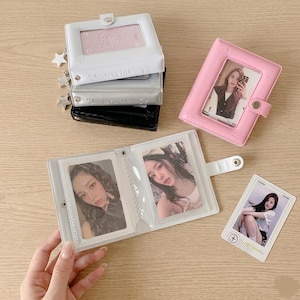 May include: A collection of small, rectangular photo card binders in white, silver, black, and pink. Each binder features a snap closure, a front display window, and star-shaped charms. The binders contain clear plastic sleeves holding portrait photographs.