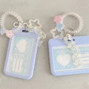 Può includere: Due porta tessere scolastiche azzurri con cinturini in plastica trasparente e portachiavi a spirale. Ogni porta tessere ha un design a cuore e le parole "SCHOOL ID CARD". I portachiavi hanno accenti di stelle e perline.