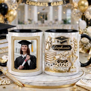 May include: White ceramic graduation mug with a black interior and handle. One side features a photo in a gold frame, the other side has graduation-themed embellishments and the name "Stephanie" and "Class of 2026".
