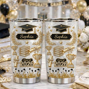 May include: Two stainless steel tumblers with a graduation theme. Each tumbler features a black graduation cap, the name "Sophia", and "Class of 2026" in gold. The design includes gold laurel wreaths, stars, books, and trophies.