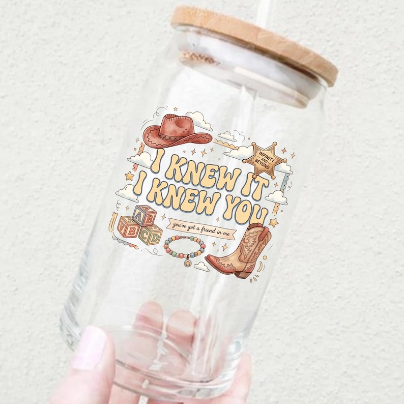 May include: A clear glass tumbler with a bamboo lid featuring a colorful graphic print of a cowboy hat, alphabet blocks, a beaded bracelet, a cowboy boot, and a sheriff star with the text I KNEW IT I KNEW YOU and you've got a friend in me.